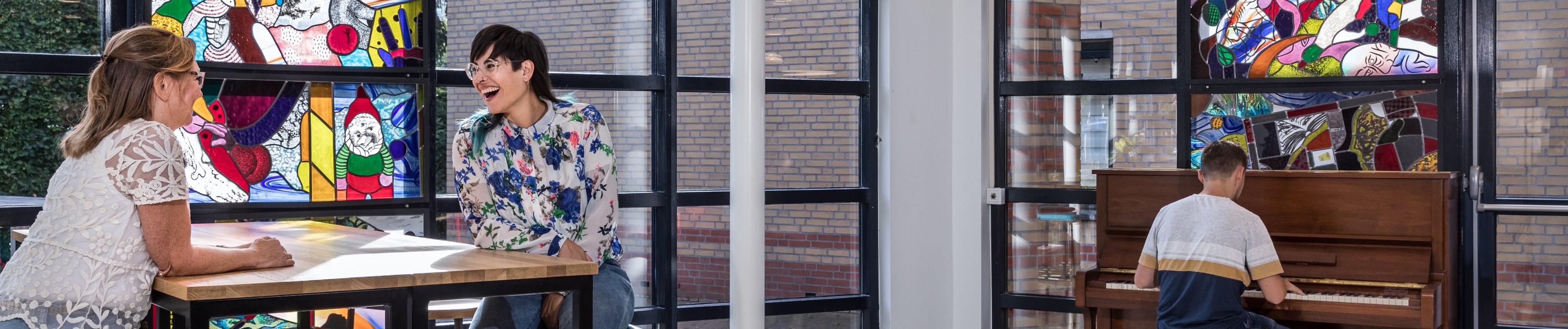 Twee vrouwen in gesprek. Man speelt piano